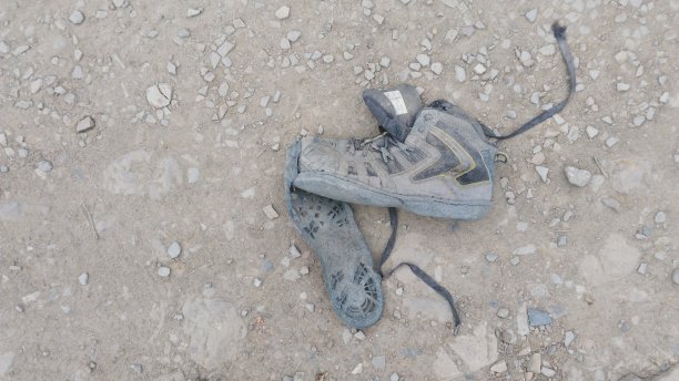 被一个无家可归的行人丢弃在泥土路上的破损鞋子图片下载