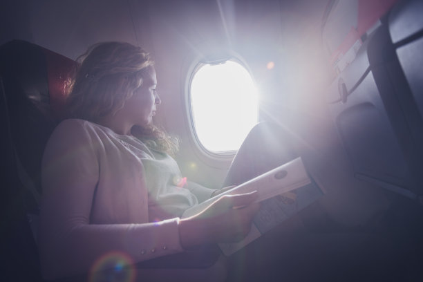在飞机上看报纸的卷毛女人。图片下载