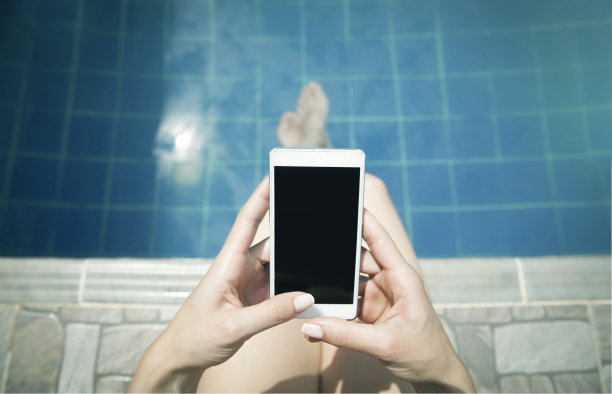 一个面面相觑的女人在泳池边放松，用智能手机聊天图片下载