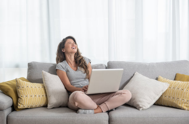 年轻漂亮的单身女人和她的男朋友或女朋友聊天坐在沙发上的笔记本电脑和大笑图片下载