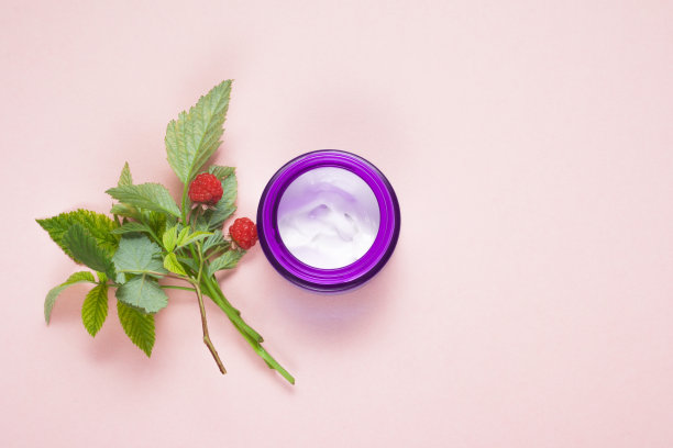 天然化妆品白色霜在一个紫色的容器，绿色的小枝和红色的覆盆子(天然成分)在粉红色的背景与复制空间。美容产品。平躺，俯视图图片下载