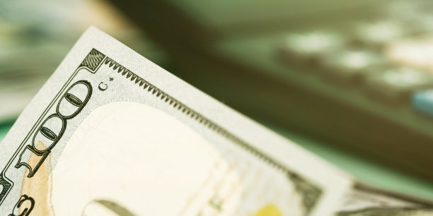 百元钞票边缘躺在模糊的计算器近旁图片下载