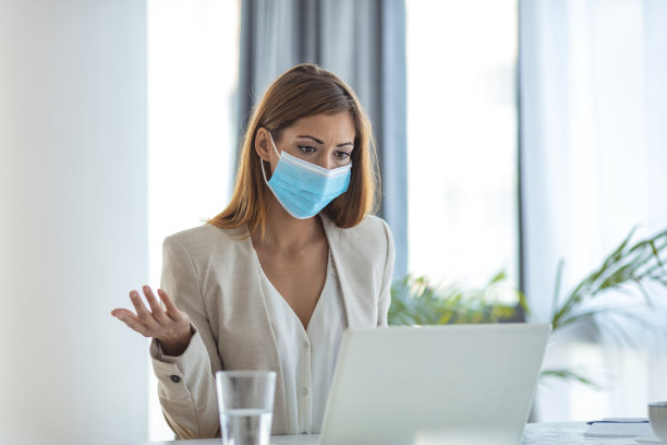 戴着防护面具在办公室用笔记本电脑工作的女商人。素材图片