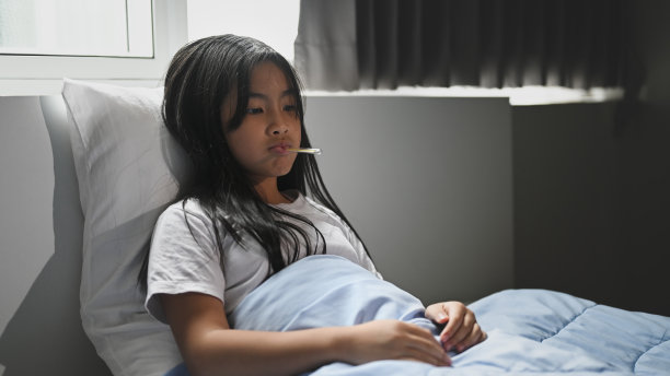 一个生病的小女孩盖着毯子躺在床上测量温度。图片下载