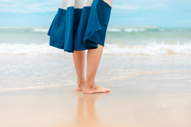 女人脚踩在沙滩上，海水流动。图片下载