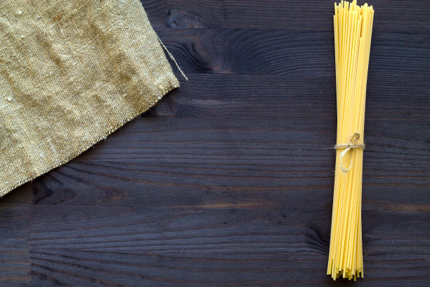 木桌上放着小麦意面。生意大利面与麻袋布在黑色背景与复制空间。前视图。意大利菜。图片下载
