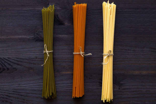 生意大利面放在一张有复印空间的木桌上。前视图。深色背景上是生的小麦、番茄和菠菜意大利面。意大利美食图片下载