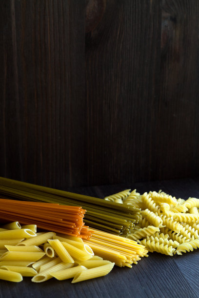 意大利菜。不同类型的意大利面放在一张有复印空间的木桌上。生菠菜意大利面，小麦意大利面和番茄意大利面，黑底通心粉。垂直图片下载