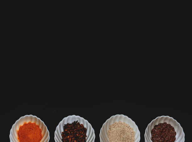 在孤立的黑色背景上，白色杯子里的香料和谷物的边缘。图片下载