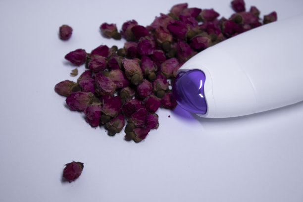 白色的洗发水瓶子，紫色的脖子，没有标签旁边一堆粉红色的玫瑰。身体护理和美容理念图片下载