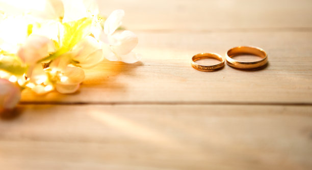 木制背景上有两个金环，上面开着白色的苹果花。图片下载