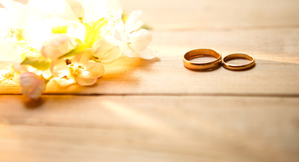 木制背景上有两个金环，上面开着白色的苹果花。图片下载