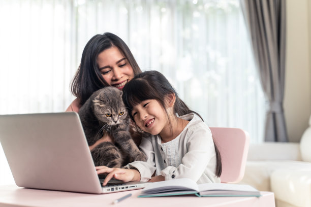 家庭学校亚洲年轻女孩学习网上和做家庭作业使用电脑上网与母亲的帮助，教和鼓励。女孩笑着和小猫一起在家里学习和玩耍。图片下载