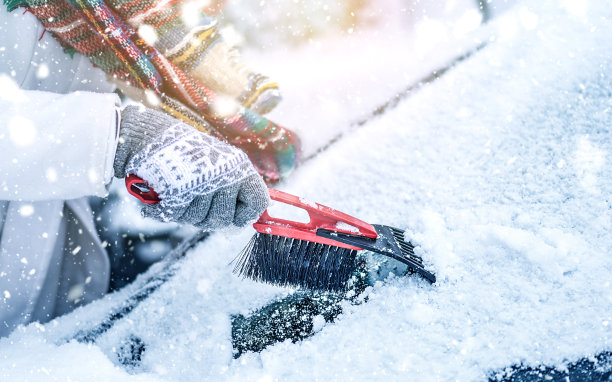 女人清理挡风玻璃上的雪，刮着冰冻的玻璃。图片下载