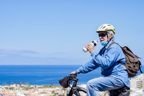 老人eisinf骑着自行车，戴着黄色头盔，高兴地结束了部分禁闭，戴着面具保持社交距离。冠状病毒尚未被打败图片下载