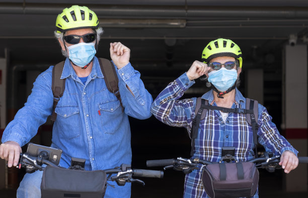 两位老年人骑着自行车，一位老人和一位老妇人，通过碰触肘部而不是拥抱或握手来互相问候。新冠疫情尚未结束图片下载