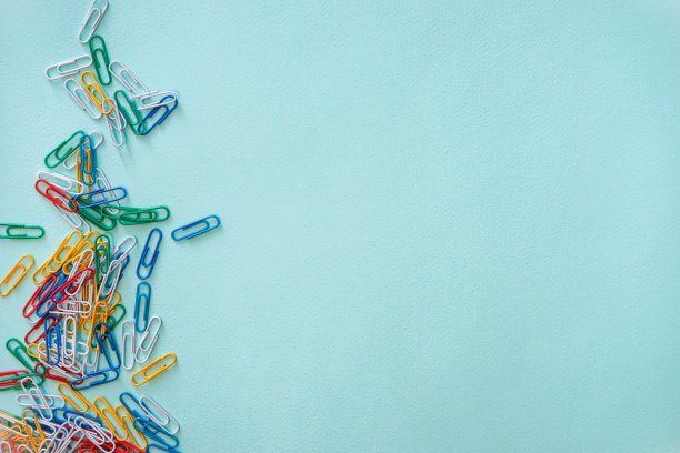水平特写平铺组成的多色回形针在浅蓝色的背景。照片左侧是一堆绿色、红色、黄色、白色和蓝色的物体。办公用品的概念。文具。水平的照片。回到学校图片下载