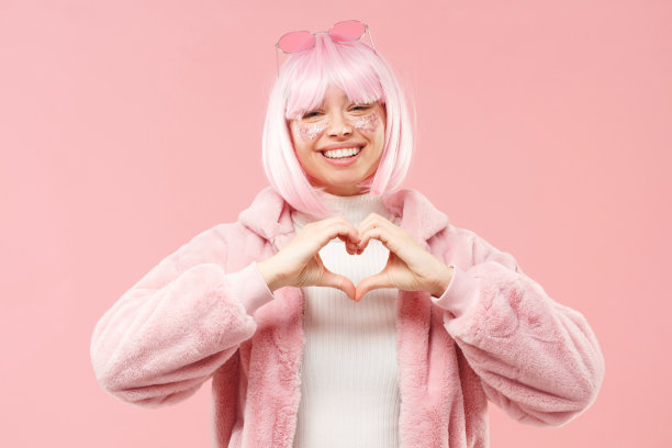 年轻女孩用手表示爱心，分享爱和欣赏，孤立在粉红色的背景下图片下载