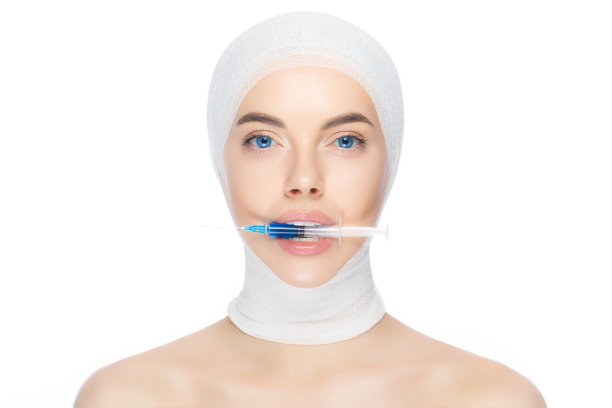 特写的年轻女性头部和颈部的医疗绷带，持有注射器在牙齿，孤立的白色背景。整形外科的概念图片下载