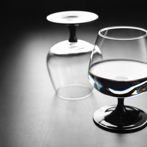 两只杯子放在一条黑腿上，一只杯子里装着水，另一只倒扣着，映衬着黑色的背景。Copyspace图片下载