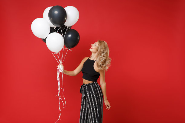 微笑的年轻女子女孩在黑色衣服摆孤立的红墙背景。情人节生日派对的概念。模拟拷贝空间。庆祝的时候把气球放在一边。图片下载