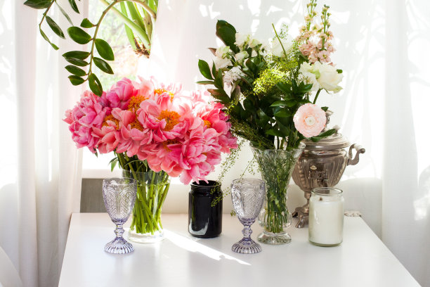 靠窗的白桌上放着牡丹和玫瑰花束、黑白蜡烛、酒杯和旧茶壶。图片下载