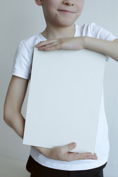 穿着白色t恤的美丽的孩子微笑着，手里拿着一块木头画板。广告的地方。特写镜头图片下载