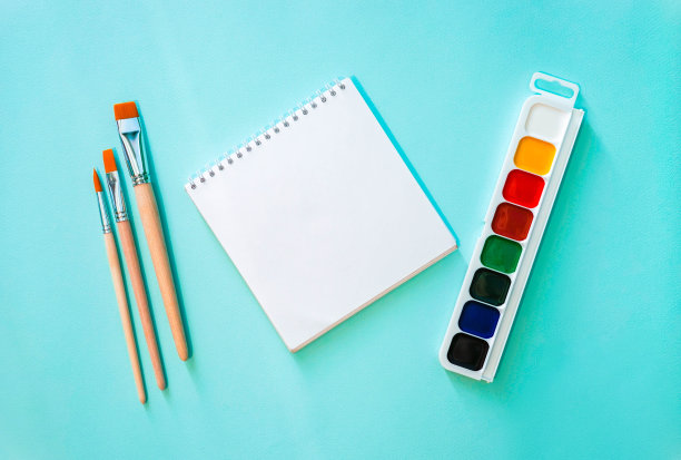 水平的极简特写平铺构图与透明纸笔记，三个浅米色笔刷与橙色堆和木制纹理和颜色水彩画在浅蓝色的背景。照片中央的物体。文具图片下载