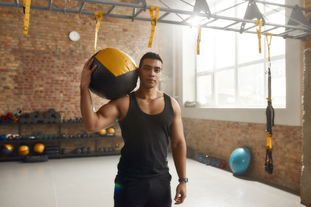 提高你的精神。在工业健身房锻炼时，手持健身球，看着摄像机的运动型男子图片下载