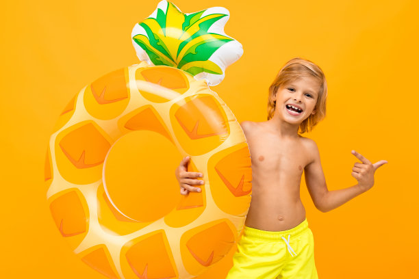 漂亮的欧洲金发男孩，穿着黄色游泳裤，橙色背景上有圆圈菠萝图片下载