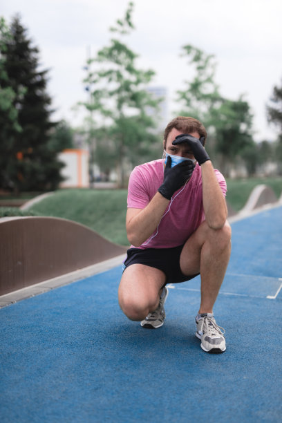 运动员戴着医用口罩和手套，智能手机和耳塞，在城市环境中慢跑。精疲力竭的男子从慢跑和医用口罩的使用。麻烦与呼吸。图片下载