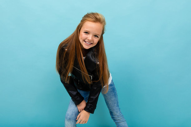 迷人的欧洲女孩在皮夹克和牛仔裤摆姿势与copyspace浅蓝色背景图片下载