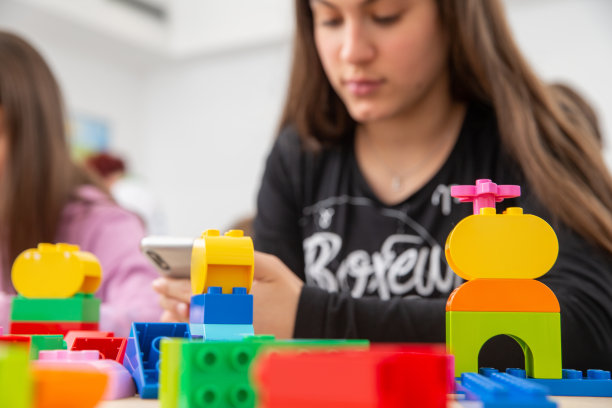 十几岁的女孩坐在教室后面的桌子上装满了玩具，但她更喜欢在她的智能手机上发短信-库存照片图片下载