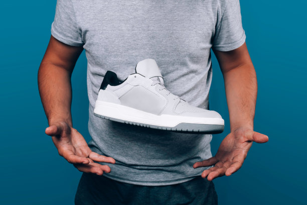 男人捧着时髦的灰色运动鞋在空中，手下靴子，运动的生活方式，呈现新型的鞋子图片下载