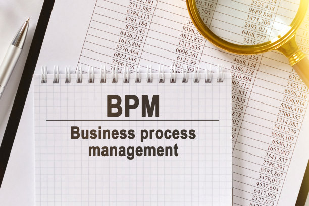 桌子上放着财务报告、一支钢笔、一个放大镜和一个刻有“BPM”字样的笔记本。图片下载