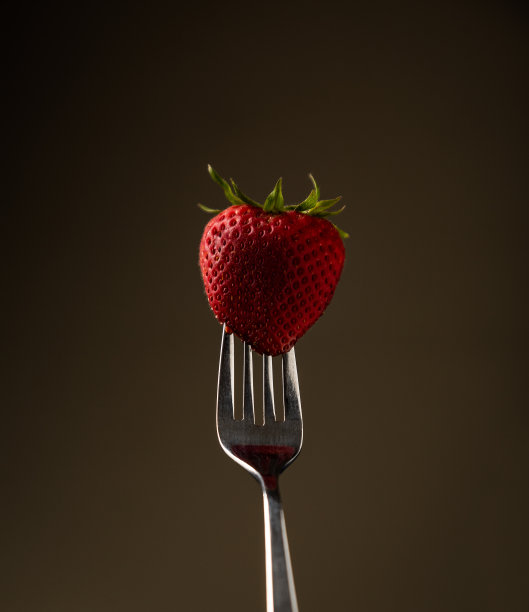 叉子上放着令人垂涎的健康草莓，映衬着米色的背景。图片下载