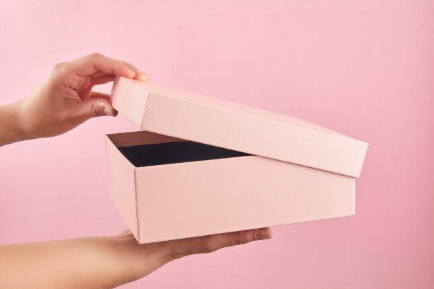 手拿着粉彩背景上的粉色纸盒包装。惊喜在打开的纸盒里。图片下载
