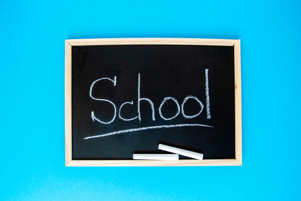 “学校”这个词是用粉笔写在一个框子里的黑色黑板上，还有两根粉笔。黑板的背景是蓝色的图片下载