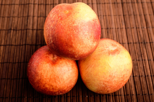 三个新鲜成熟的有机油桃放在一张棕色的木桌上，俯视图或平放健康水果的照片图片下载