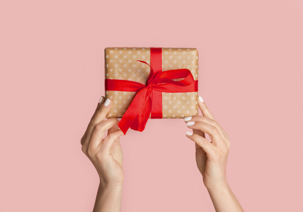 千禧女孩拿着包装的礼物与红色丝带的节日场合，粉红色的背景，特写图片下载
