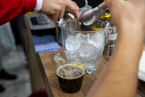 一只手拿着钳子从花瓶里取出冰块，放进一个塑料玻璃杯里，和刚煮好的黑咖啡一起。特写，软焦点，模糊背景图片下载