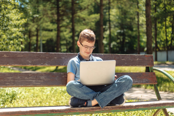 一个在公园长椅上拿着笔记本电脑的少年。远程学习。学习在任何地方。图片下载