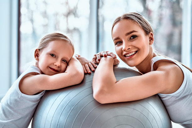 年轻漂亮的妈妈和她的女儿一起坐在健身球旁边的地板上，手里拿着哑铃素材图片