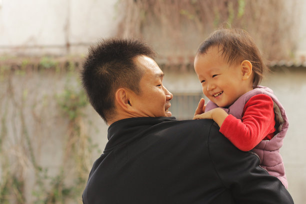 一个微笑的亚洲父亲抱着他的女儿在一座老房子前。图片下载