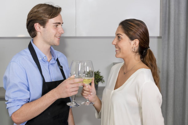 年轻夫妇在厨房里互相微笑，用两杯白葡萄酒敬酒图片下载