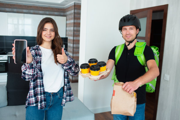 送餐员给一位住在她家的年轻女士送餐。他们都看着镜头笑了。图片下载