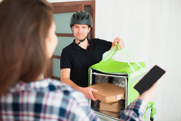 食品配送的概念。送餐员给年轻女子送餐。她想用智能手机上的应用程序支付订单。图片下载