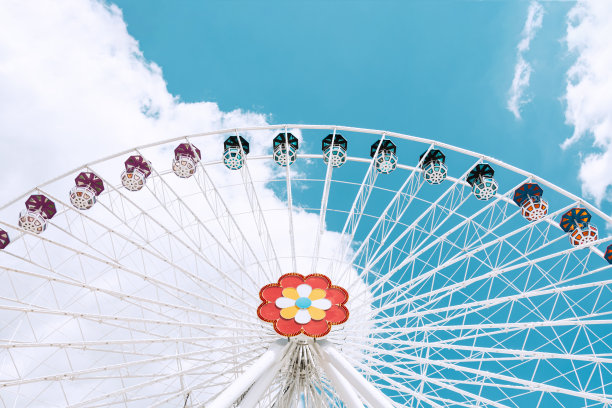 一个白色的摩天轮和不同颜色的小屋映衬着蓝色的天空。图片下载