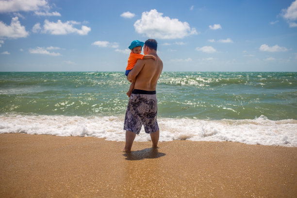 在沙滩上，爸爸抱着一个蹒跚学步的孩子图片下载