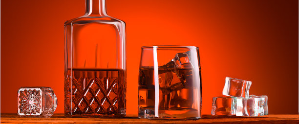 一杯威士忌或白兰地，一个醒酒器和冰块，放在一张木桌上。图片下载